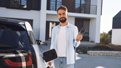 man with an electric car charger in his hand outside an apartment