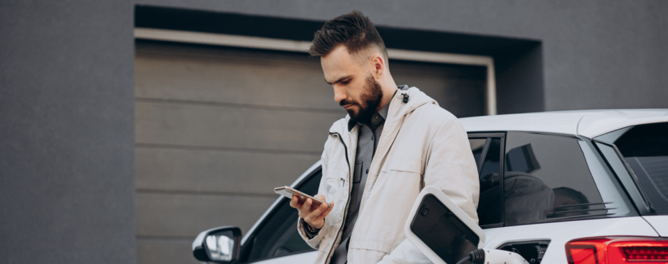 man laddar sin elbil och tittar på sin telefon